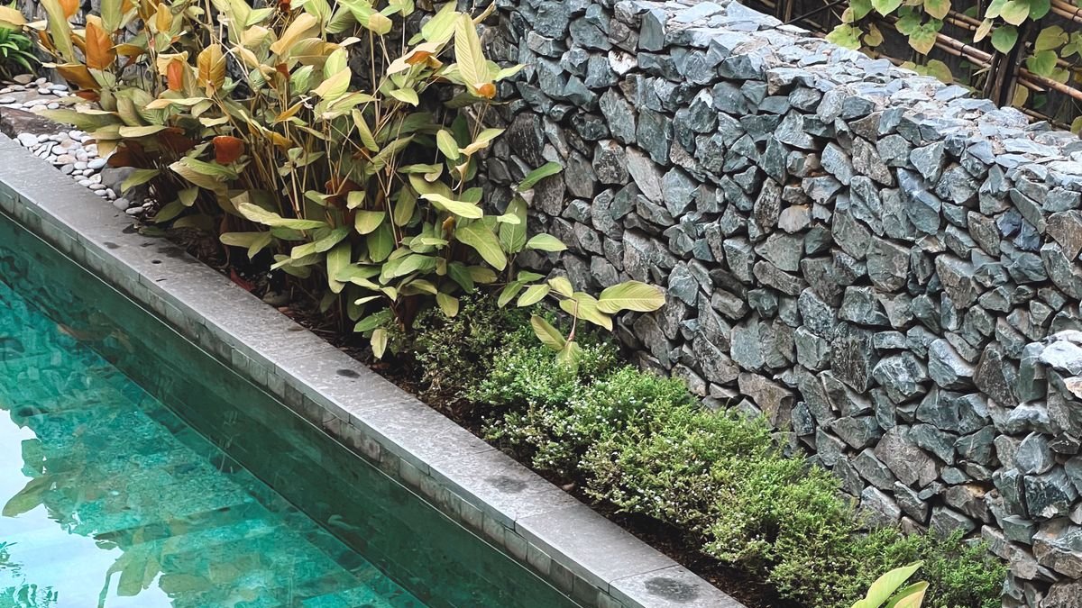 Stone retaining wall running alongside a concrete pool edge